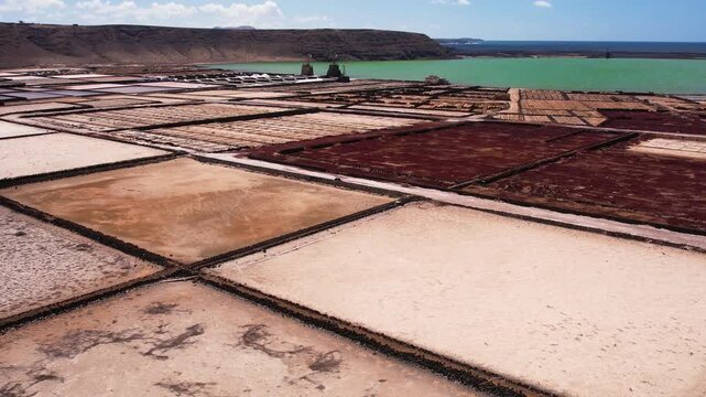 Explore the unique salt pans of Lanzarote. Observe the layout and structure of the salina, with the ocean and landscape in the background