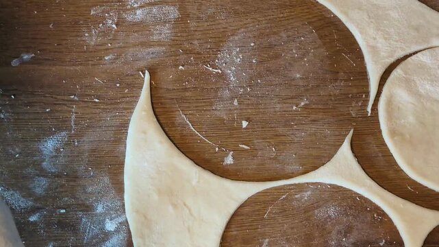 Close-up vertical shot of a woman making traditional Polish pierogi dumplings completely by hand, adding fresh potato cheese filling with a spoon on a rustic flour-dusted wooden kitchen table