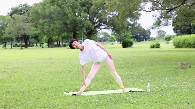 公園でヨガの三角のポーズを行う笑顔のアクティブシニア女性