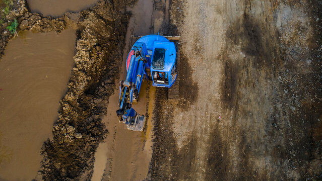 Aerial view of a blue excavator operating on a muddy construction site with brown earth and puddles Karanglewas, Central Java, Indonesia.