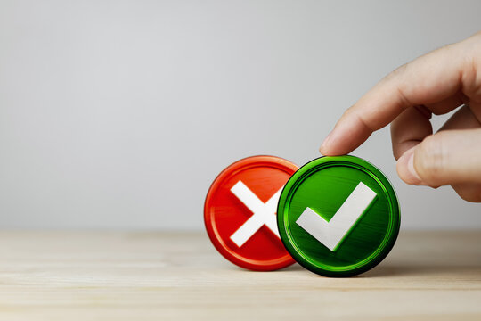Hand choosing green checkmark over red cross icon block on desk with copy space. Right decision, correct choice, business approval, do and donts, true or false presentation concept. Minimalist.