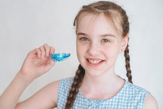 Smiling little girl holding a silicone dental mouthguard for orthodontic bite correction, pediatric dentistry concept