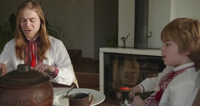Man With Kid Boy Eat Food Lunch Dinner. Family in Ukrainian Traditional Attire Childhood. 4K 10-bit