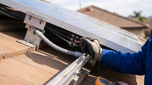 Renewable Energy Technician Checking Wiring Beneath Rooftop Solar Panels, Testing Meter, Roof Brackets, Clean Energy