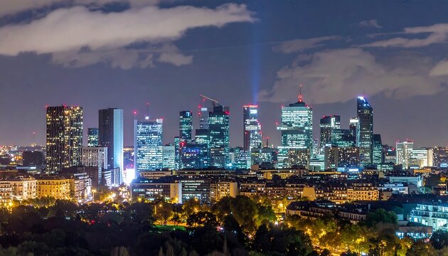 A nighttime cityscape with a cluster of illuminated skyscrapers standing tall amidst smaller buildings, with two beams of light shooting up into the dark sky