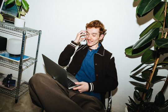 Young man producing music on laptop with headphones at home