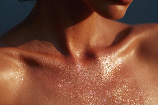 Close up of glistening water droplets on skin with visible sunscreen sheen, highlighting the texture and contours of the shoulders and collarbone area in natural light