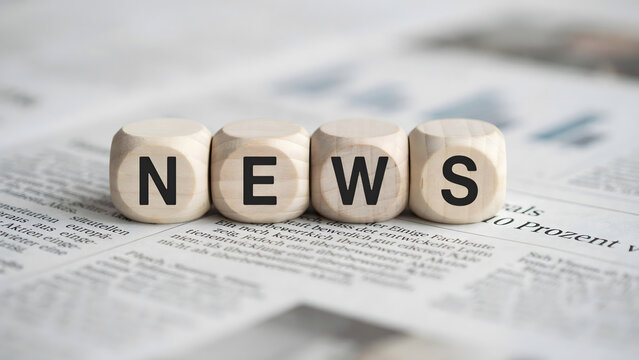 Wooden blocks with letters spelling news on a blurred newspaper background