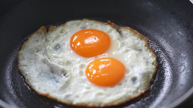 sunny-side-up fried eggs cooked in a black pan, featuring vibrant orange yolks and perfectly cooked egg whites with slightly crispy edges. This simple high-protein breakfast dish is ideal for homemade