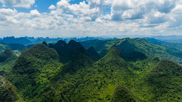 Aerial view of the lush karst mountains and limestone peaks at Ruyi Peak ropeway scenic area under a cloudy blue sky in Yangshuo, Guangxi, China.