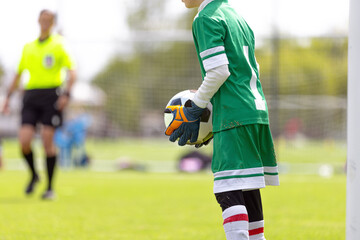 Naklejka premium Young Goalkeeper Holding Ball: Youth Soccer Player in Green Uniform Preparing for Goal Kick
