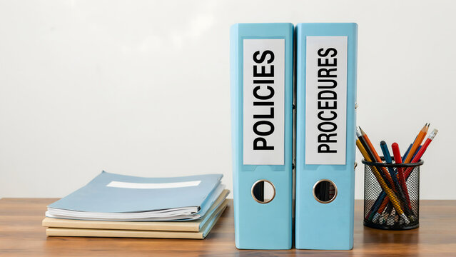 Two light blue binders labeled policies and procedures on an office desk