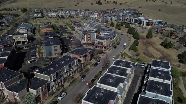 Clustered townhome rows along Laramie Blvd beside Uptown Broadway, foothill slopes frame western edge of North Boulder. Flat roofs, varied facades, aligned parking, sharp midday contrasts, CO