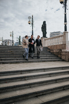 Three business colleagues walk down stone steps carrying documents and talking. A winter business meeting continues outdoors as professionals descend stairs near statues.
