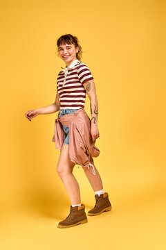 Young woman joyfully posing in stylish summer outfit against vibrant yellow backdrop