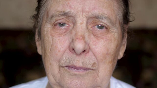 Shot of elderly woman face with sorrowful expression, showing deep wrinkles and age spots as tears well up in eyes, evoking feelings of sadness. Old lady suffers from tremor and eyelid twitching