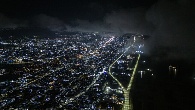 Aerial view of the illuminated Coastal Road and city lights at night with misty clouds over the shoreline in Lekki, Lagos, Nigeria.