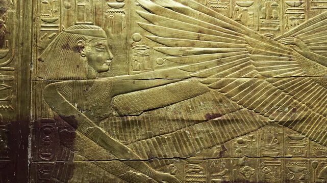 Closeup of golden Tutankhamun shrine panel with goddess and mummified figures relief.