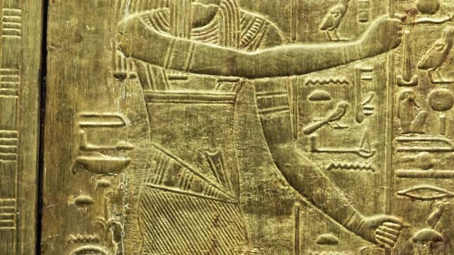 Closeup of golden Tutankhamun shrine panel with goddess and mummified figures relief.