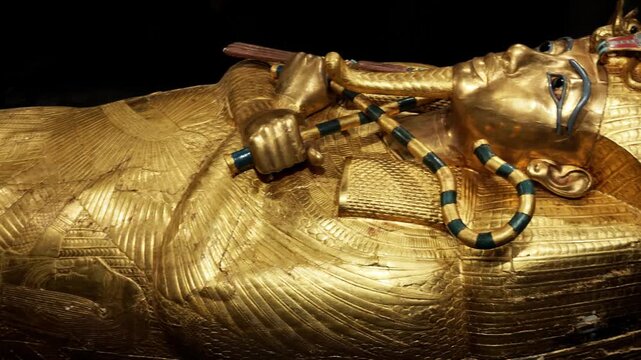 Extreme closeup of Tutankhamun solid gold inner coffin with crook scepter and blue inlay details on black background. Priceless royal Egyptian treasure.