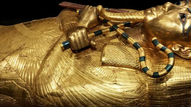 Extreme closeup of Tutankhamun solid gold inner coffin with crook scepter and blue inlay details on black background. Priceless royal Egyptian treasure.