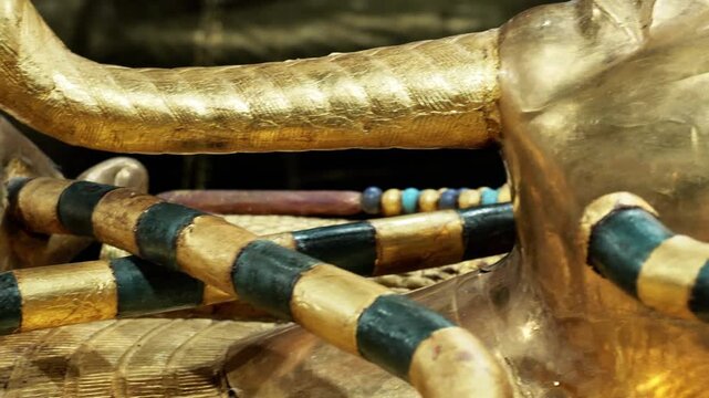 Extreme closeup of Tutankhamun solid gold inner coffin with crook scepter and blue inlay details on black background. Priceless royal Egyptian treasure.