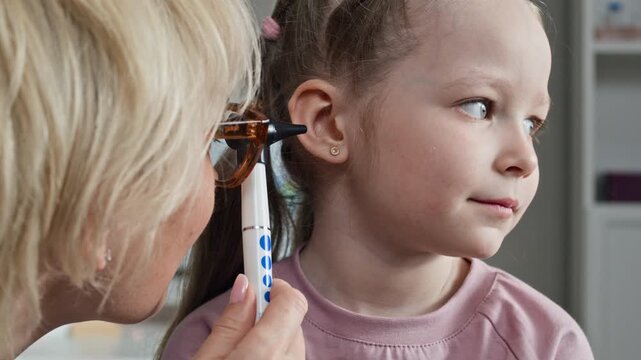 Closeup of middle aged Caucasian female pediatrician examining ear of Caucasian child girl using otoscope during medical checkup. Clip is perfect for pediatric healthcare and family clinic advertising