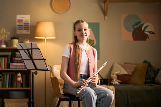 Portrait of Caucasian girl studying music and holding flute during home practice, representing arts education and skill development. Useful for music lessons, tutoring, youth learning