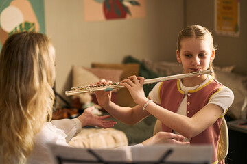 Caucasian girl playing flute during music lesson with teacher, practicing instrument technique and arts education. Useful for school programs, tutoring, youth learning campaigns © DragonImages