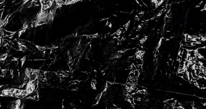 Close-up of shiny dark crinkled surface with sharp folds and reflective highlights. Smooth continuous rotation reveals dynamic shifts in deep shadows and bright specular reflections.