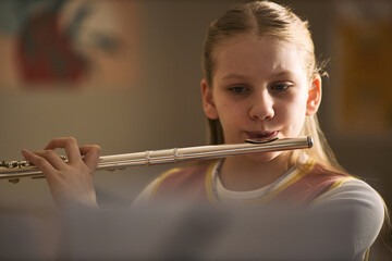Caucasian girl playing flute during music lesson, practicing instrument skills and arts education. Useful for school programs, music classes, youth learning campaigns © DragonImages