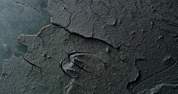 Rough surface with thick cracked layers and peeling flakes. Smooth continuous rotation reveals evolving light reflections and shifting surface details across the textured plane.