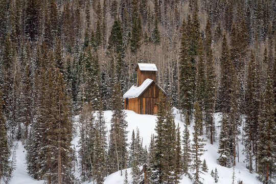 Aerial view of a historic wooden mining structure surrounded by snow-covered evergreen trees in a dense forest in Ouray, Colorado, United States.