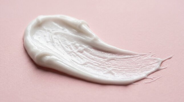 Close up of a white cosmetic cream swatch on a pink background.