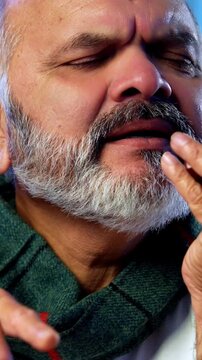 Indian senior man speaking on phone using smartphone at home at table, happy elderly person having cheerful conversation while seated indoors in casual setting during relaxed retirement lifestyle