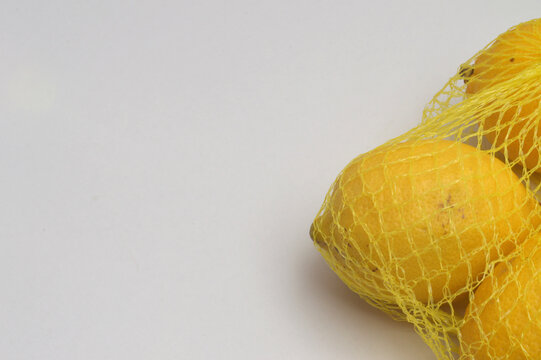 yellow lemon in a yellow mesh  on a white background corner composition horizontal layout, lemons close up with generous copy space,