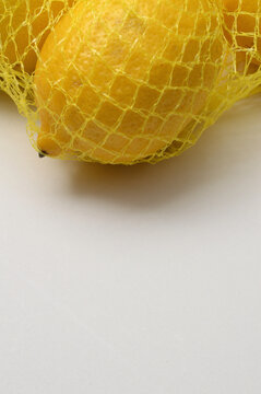yellow lemon in a yellow mesh  on a white background corner composition vertical layout, lemons close up with generous copy space,