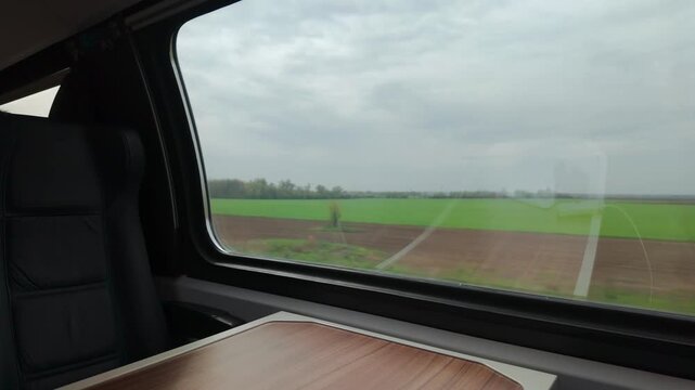 Interior of a train cabin with a wooden table beside a large window revealing green fields and a calm travel moment.