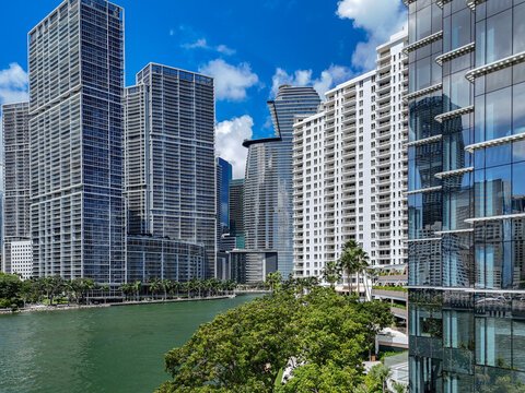 Aerial view of modern skyscrapers and glass towers of Downtown Miami along the river with lush green trees under a blue sky in Miami, Florida, United States.