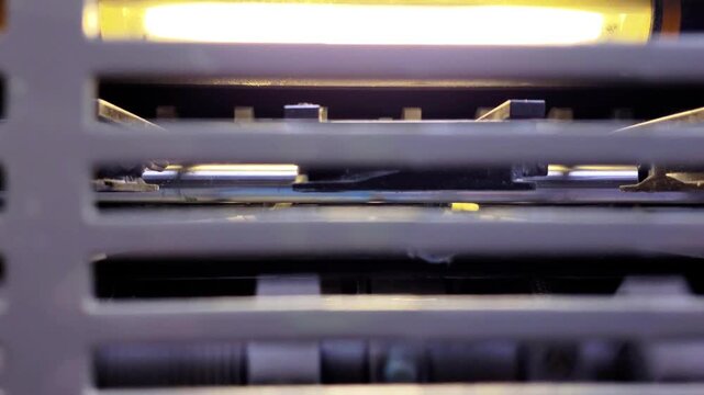 Close-up view of the mechanical rollers and guide system moving color-printed paper through an industrial printing machine at high speed.