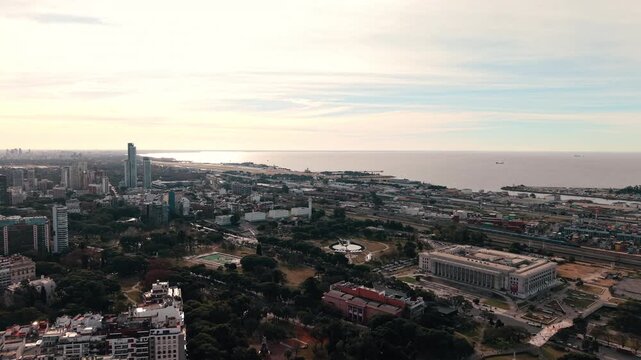 Forward aerial approach, framing the UBA Law School next to an airplane descending towards Aeroparque over Rio de la Plata.