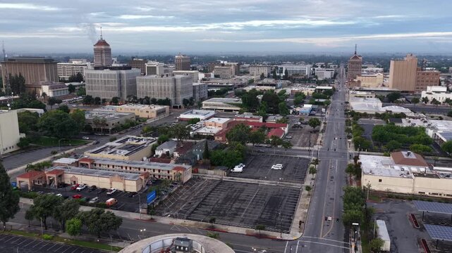Fresno skyline rises above California&rsquo;s Central Valley, with wide boulevards, parking lots, mixed-use buildings and overcast skies over downtown Fresno, California, USA. Aerial drone wide shot.