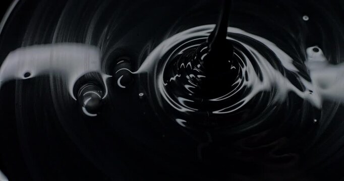 Black viscous liquid fast spiral. Close-up of thick black fluid flowing in rapid swirling spirals with white highlights. 
