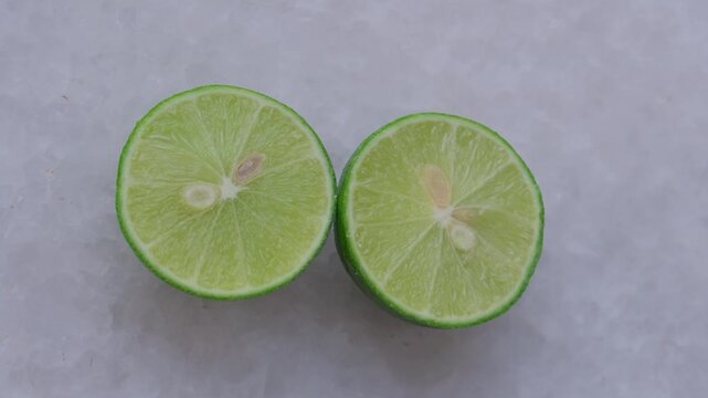 Close-up of two fresh lime halves placed on a textured white surface