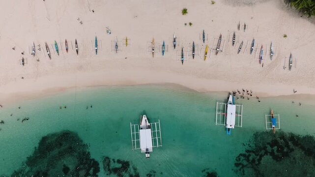 Row of colorful fishing boats on white sandy beach near turquoise water. Daku Island. Siargao, Philippines.