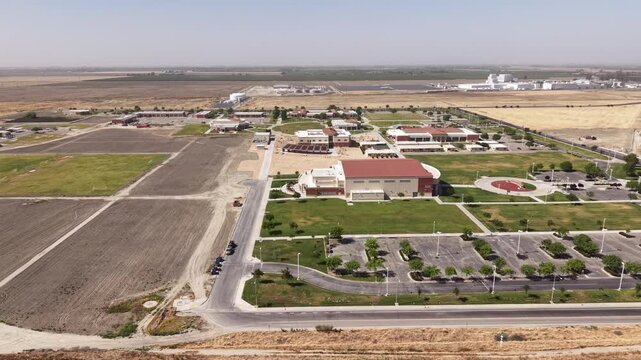 Tracking view from a drone showing the sprawling campus of West Hills College in Lemoore, California, surrounded by agricultural fields and flat rural landscape on a clear sunny day