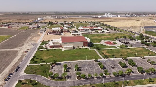 Drone zoom out of the West Hills College Lemoore campus on a sunny day in the California Central Valley. Showing modern university buildings, green lawns and the surrounding farmland
