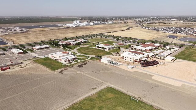 Panning drone view showing the campus of Lemoore College in central California, with its modern buildings, green spaces, and surrounding agricultural fields under a clear blue sky