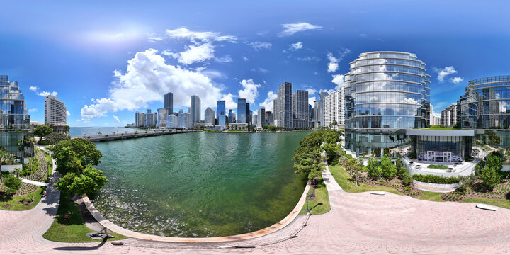 Aerial view of the modern skyscrapers and glass architecture of Downtown Miami along the waterfront under a bright blue sky with clouds in Miami, Florida, United States.