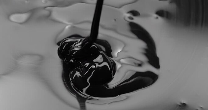 Black viscous liquid fast spiral. Close-up of thick black fluid flowing in rapid swirling spirals with white highlights. 